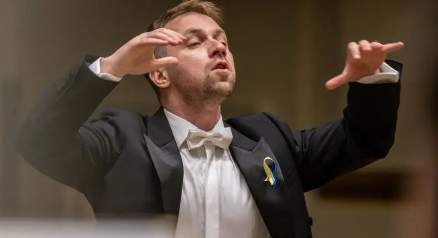 Dyrygent w garniturze z kokardką, prowadzący wykonanie Carmina Burana, z ukraińską wstążką na klapie.