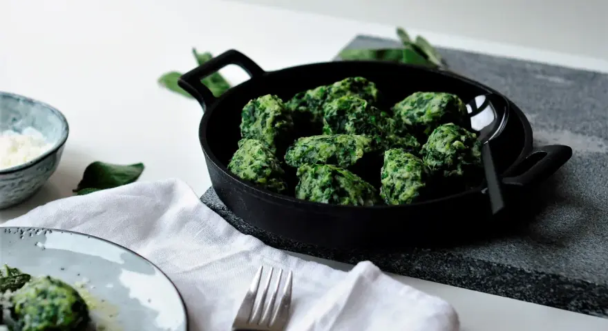 Malfatti, was ist das? Grüne, unregelmäßige Klößchen aus Spinat und Ricotta in einer Pfanne, daneben ein Teller mit mehr Malfatti und Parmesan.