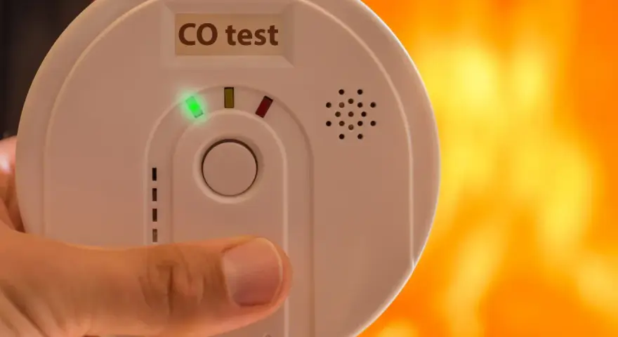 Detektor czadu z zieloną diodą i napisem "CO test" na tle płomieni.