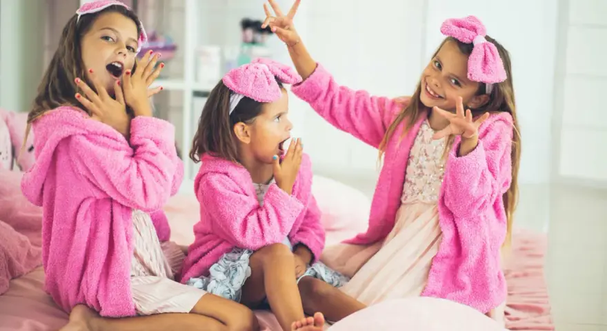 Tre glada tjejer i rosa morgonrockar och rosetter på huvudet har ett härligt spa kalas.