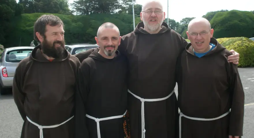 Four monk priests in brown robes stand together outdoors.