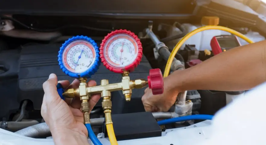 A mechanic uses a manifold gauge set to check for a freon leak in a car's AC system.