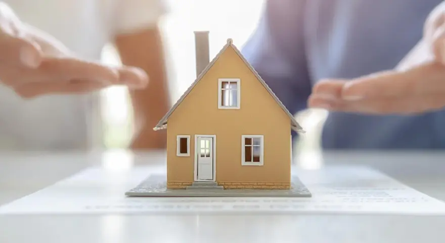 Modèle de maison sur des documents, mains en arrière-plan suggérant une solution pour sortir de l'indivision sans vendre.