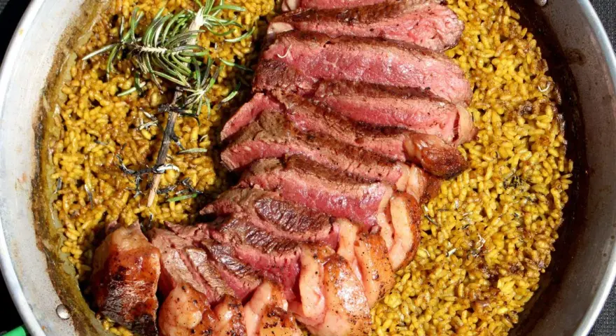 Arroz amarillo con chuletón a la parrilla y romero en paellera.