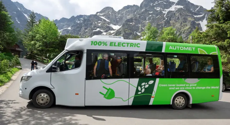 Elektryczny bus na Morskie Oko, z pasażerami w środku, na tle gór.