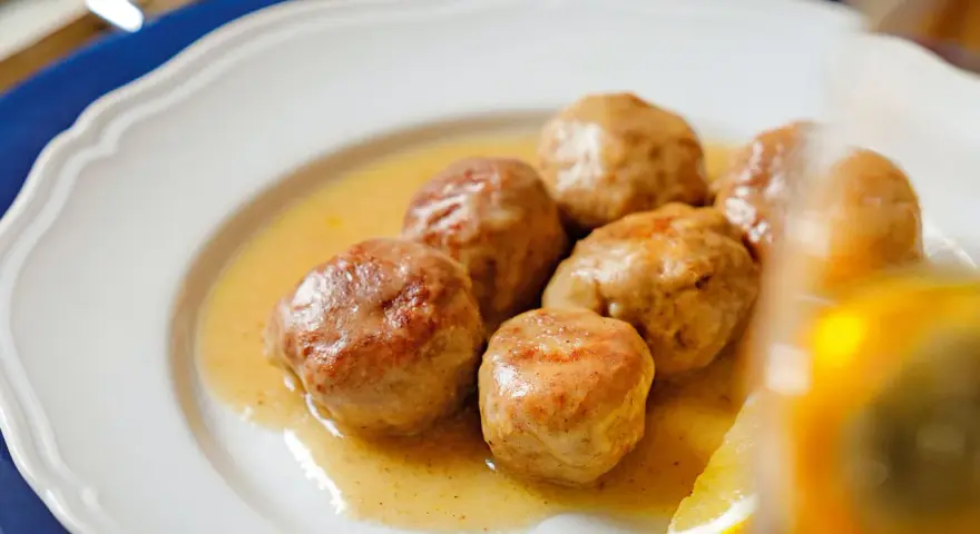 Polpette al limone succulente in un piatto bianco, con una fetta di limone e basilico.