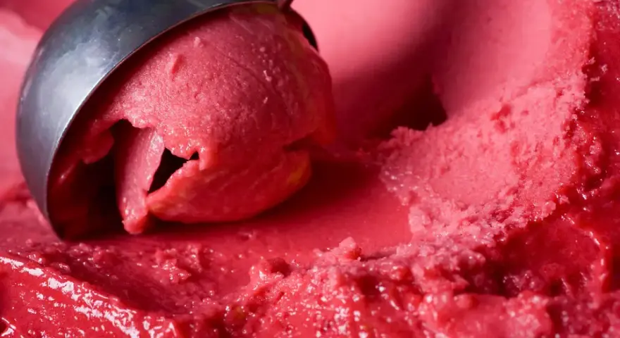 Ein Löffel nimmt eine Kugel leuchtend rotes Eis auf. Es sieht aus wie ein köstliches Blaubeereis, das zum Genießen bereit ist.