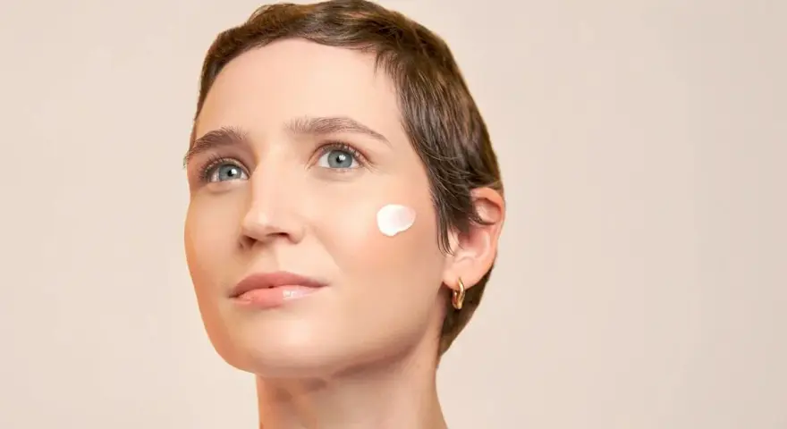 Une touche de crème solaire avant ou après crème hydratante sur la joue d'une femme au regard pensif.