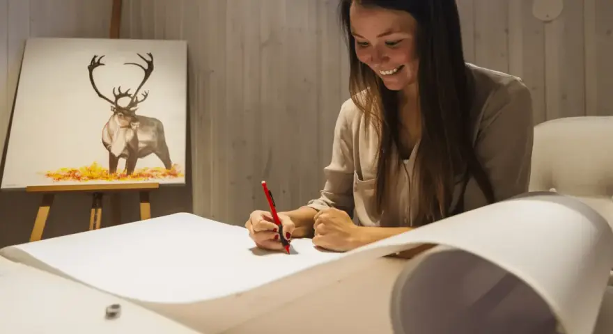 En kvinna ritar av en ren som är målad på en duk. Hon använder en röd penna och ett stort papper, en perfekt kroki modell.