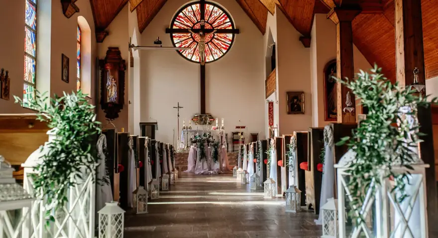 Piękna dekoracja kościoła na ślub samemu: lampiony, zielone gałązki i białe tkaniny tworzą romantyczną atmosferę.