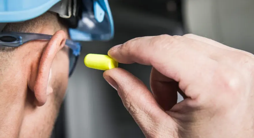 Main tenant, casque bleu, lunettes de protection et bouchon d'oreille jaune pour se protéger d'un bruit de 120 décibels équivalent.