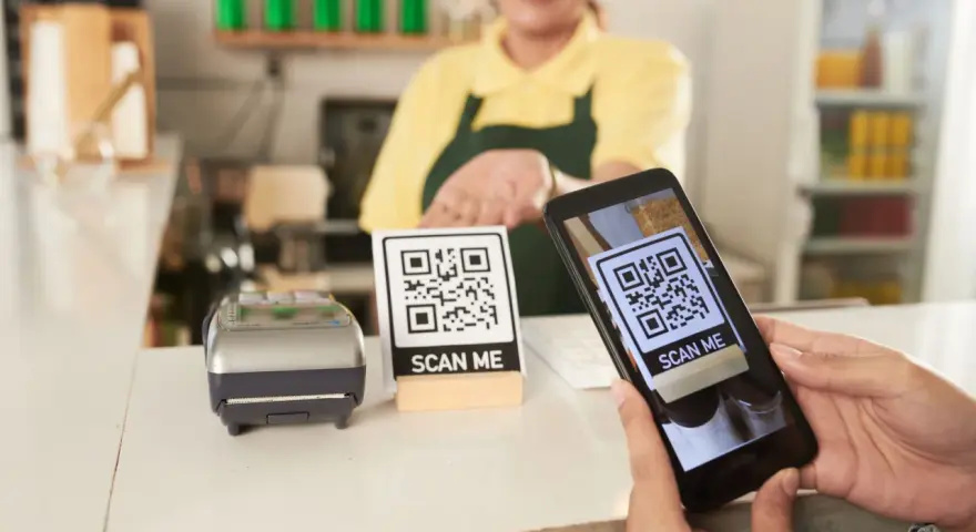 Cliente usa su móvil para escanear un código QR y hacer su carta digital. Un datáfono y otro código QR esperan en el mostrador.