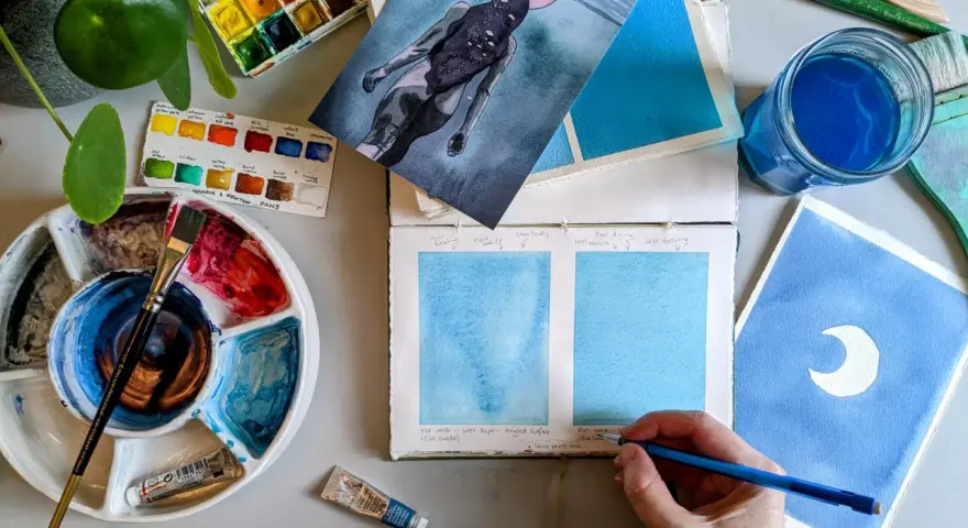 Paleta de acuarelas, pinceles y muestras de pintura azul. Un artista experimenta con técnicas de pintar acuarela.