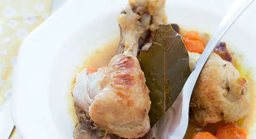 Delicioso pollo guisado con zanahorias y hoja de laurel en un plato blanco, listo para ser disfrutado.