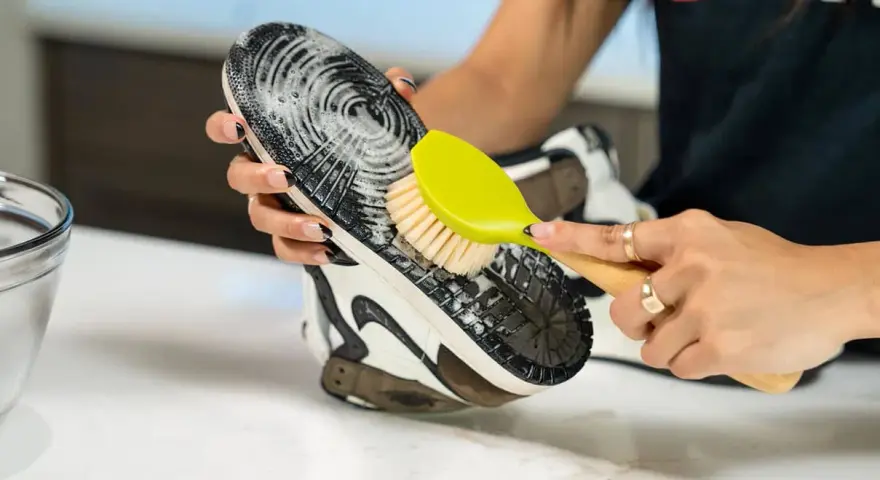 Mani che puliscono la suola di una scarpa con una spazzola gialla e schiuma. Un modo efficace per capire come pulire la suola delle scarpe.