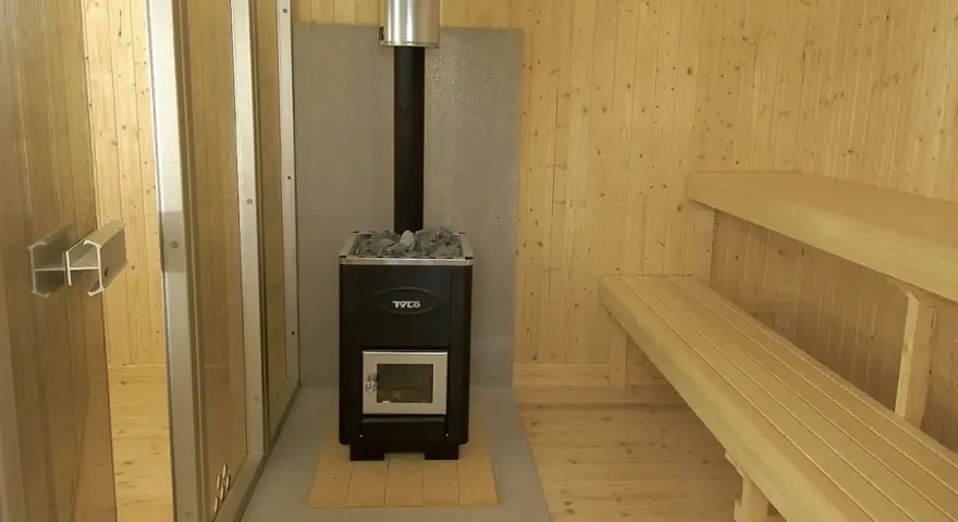 En nybyggd bastu utomhus med vedkamin, stenar och träbänkar. Perfekt för avkoppling.