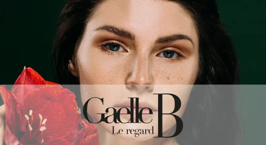 Un visage de femme avec des taches de rousseur naturelles, tenant une fleur rouge. Le regard est intense.