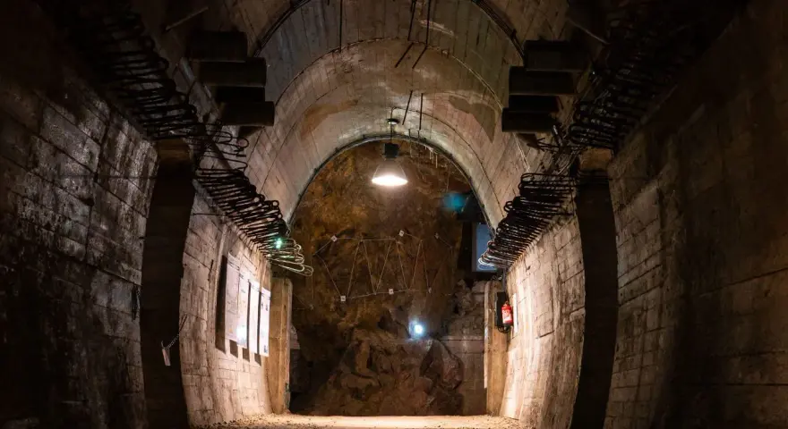 Wnętrze tunelu w Górach Sowich. Betonowe ściany, łukowe sklepienie i oświetlenie tworzą mroczny klimat.