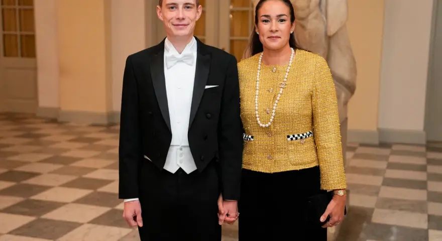 Jonas Vingegaard and his wife, Trine Marie, dressed formally for an event. He wears a tuxedo, and she sports a yellow tweed jacket and pearl necklace.