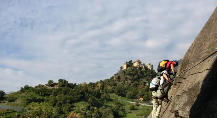 Zwei Kletterer am hoachwool Klettersteig mit Burg im Hintergrund.