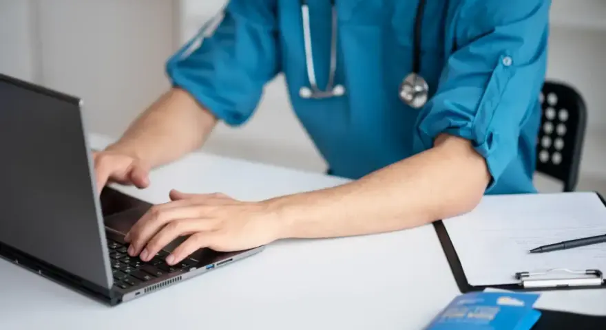Lekarz medycyny pracy na laptopie, przygotowuje dokumentację. Zastanawiasz się, ile trwa wizyta u lekarza medycyny pracy?