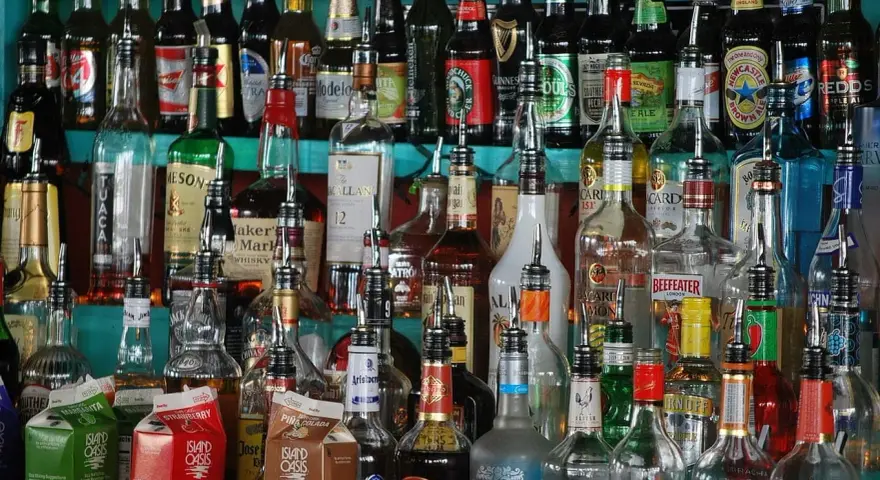 Różnorodne butelki alkoholi, w tym whisky, stoją na półce. Wskazówki, jak przechowywać whisky, mogą być przydatne przy tak bogatym asortymencie.