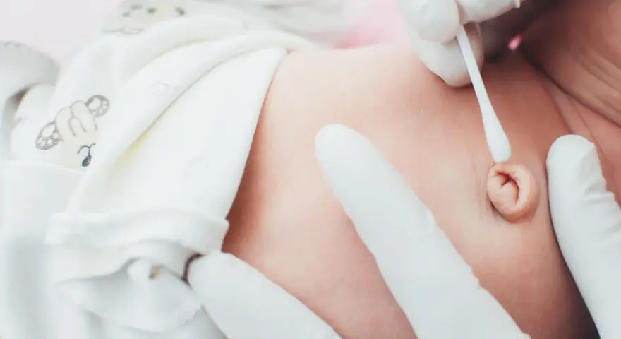 Delikatne czyszczenie kikuta pępowiny noworodka wacikiem przez ręce w białych rękawiczkach.