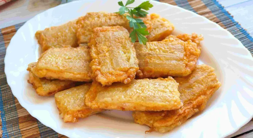 Pencas rellenas doradas y crujientes, apiladas en un plato blanco, con una ramita de perejil fresco.