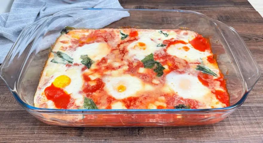 Uova alla contadina appena sfornate in teglia di vetro, con pomodoro e basilico.