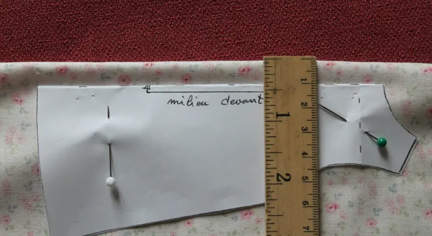 Patron de couture marqué "milieu devant", épinglé sur un tissu fleuri. Une règle en bois mesure la pièce.