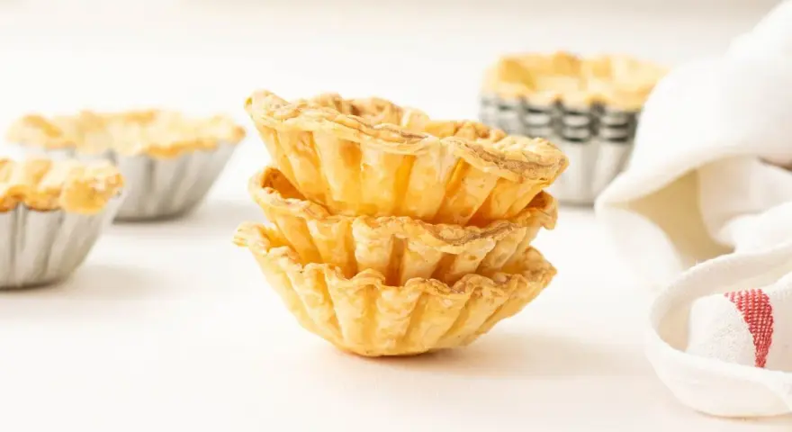 Montón de tartaletas de hojaldre listas para rellenar con crema pastelera.