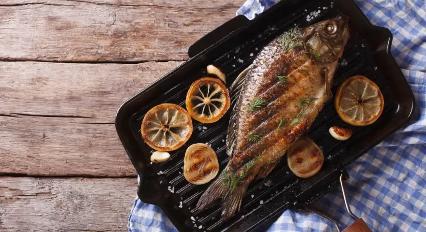 Gegrillter Karpfen mit Zitronenscheiben und Kräutern auf einer Grillpfanne. Ein Genuss, Karpfen zu essen!
