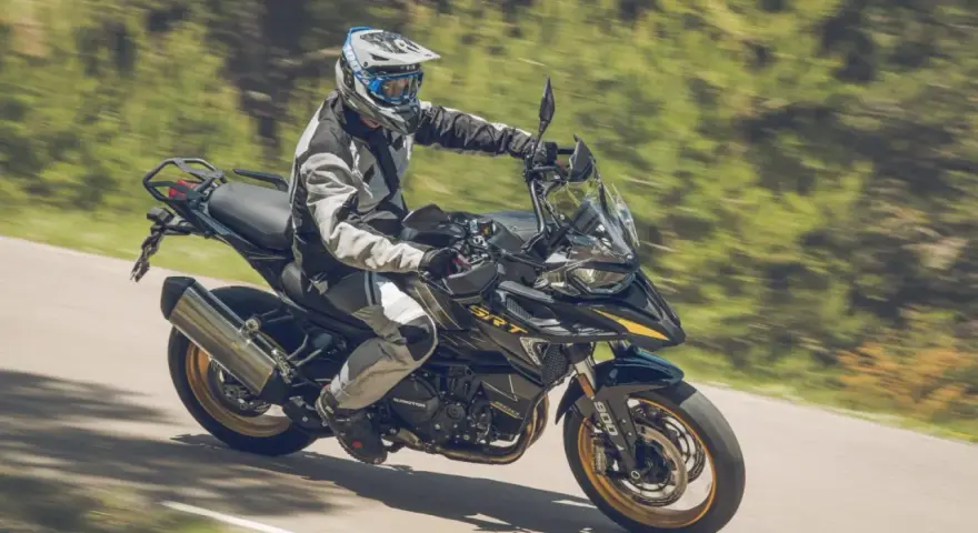 Motociclista con equipo de protección conduce una de las motos trail media cilindrada por una carretera rodeada de vegetación.