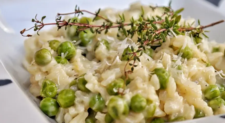 Kremowe risotto z groszkiem, posypane parmezanem i udekorowane gałązką tymianku. Pyszne danie, które zachwyca smakiem.
