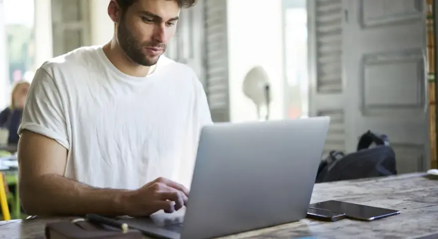 Mężczyzna w białej koszulce pisze na laptopie, przygotowując wniosek o urlop na poszukiwanie pracy.