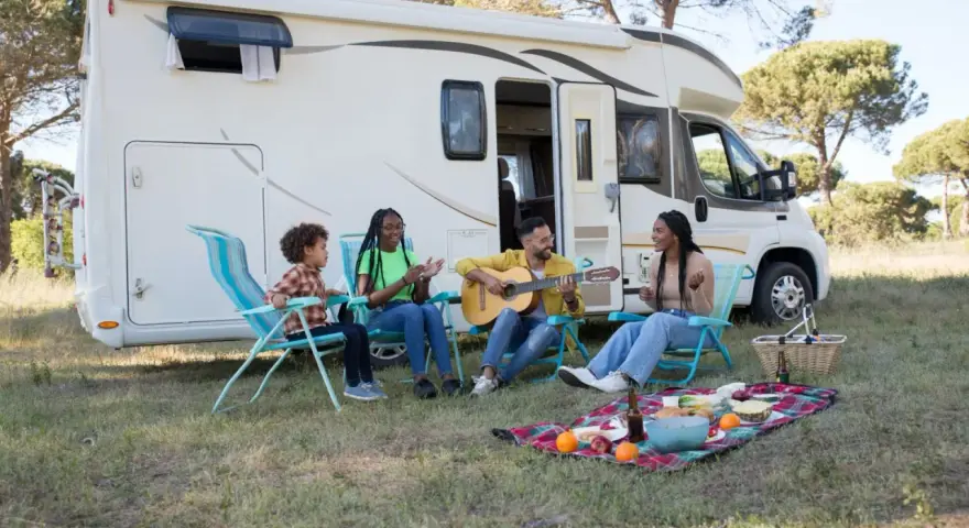 Eine Familie genießt das Camping mit Musik und Picknick vor ihrem Wohnmobil.