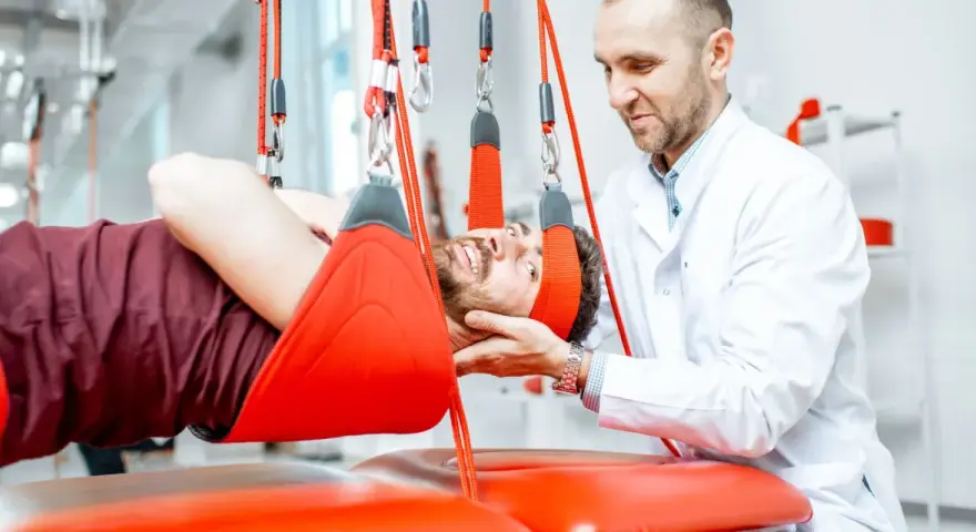 Fizjoterapeuta pomaga pacjentowi w terapii wiszącej, która może być jednym z zabiegów rehabilitacyjnych na kręgosłup lędźwiowy.