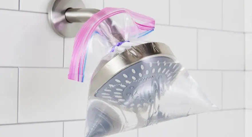A shower head is submerged in a plastic bag filled with vinegar, secured with a rubber band. This shows how to clean shower head vinegar for a sparkling finish.