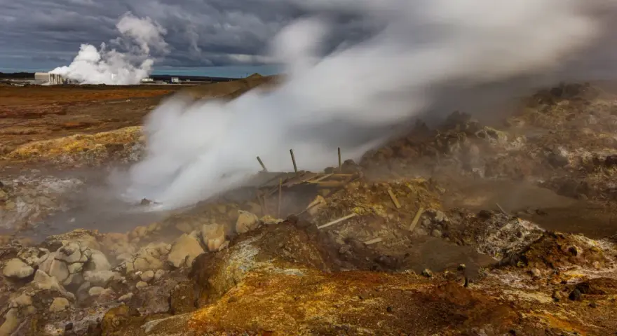 Gunnuhver hot springs: para buchująca z ziemi, zniszczona drewniana konstrukcja, chmury burzowe nad krajobrazem.