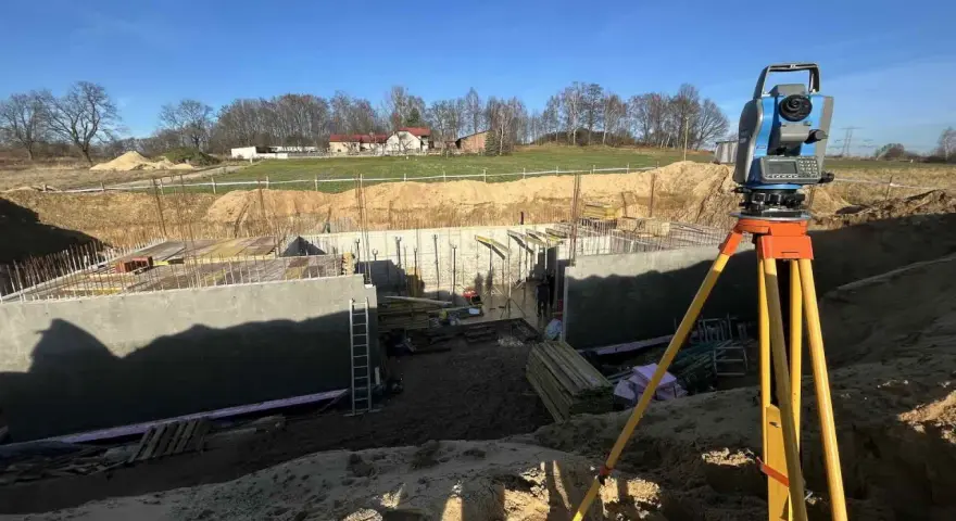Precyzyjne pomiary geodezyjne na budowie fundamentów. Totalna stacja na statywie gotowa do pracy.