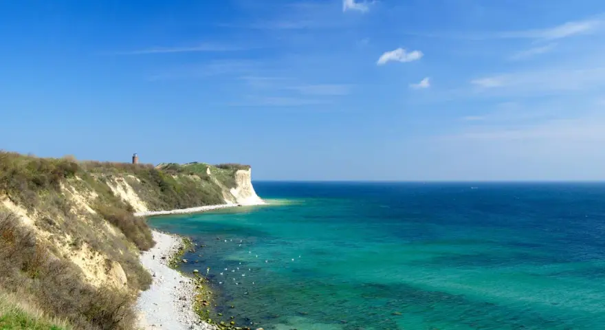Türkisblaues Meer und Kreidefelsen am Kap Arkona. Ein Leuchtturm wacht über die Küste.