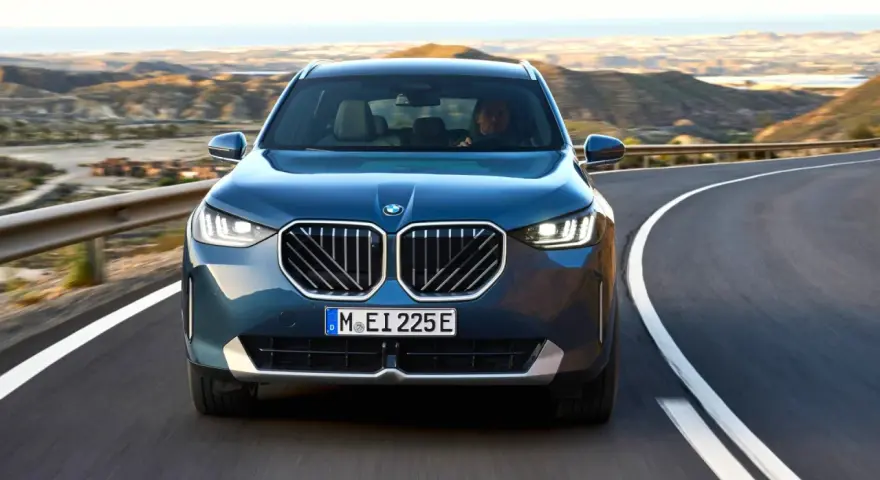 Nowy **BMW X3 2025** w kolorze granatowym jedzie krętą drogą pośród pustynnych krajobrazów.
