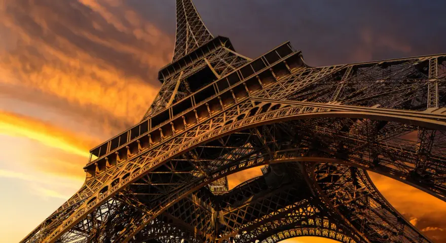 La Torre Eiffel, una icónica estructura de hierro forjado, se alza majestuosa contra un cielo anaranjado al atardecer.
