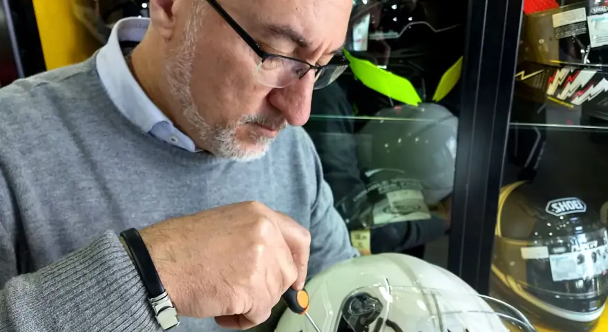 Uomo con cacciavite regola la visiera di un casco bianco, assicurandosi che il casco debba avere la visiera priva di graffi.