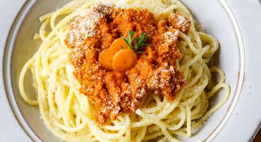 Spaghetti Bolognese, zubereitet im Thermomix, mit Karottenscheiben und Petersilie garniert.