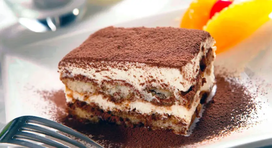 En bit krämig tiramisu, pudrad med kakao, serveras med frukt. Perfekt dryck till tiramisu.