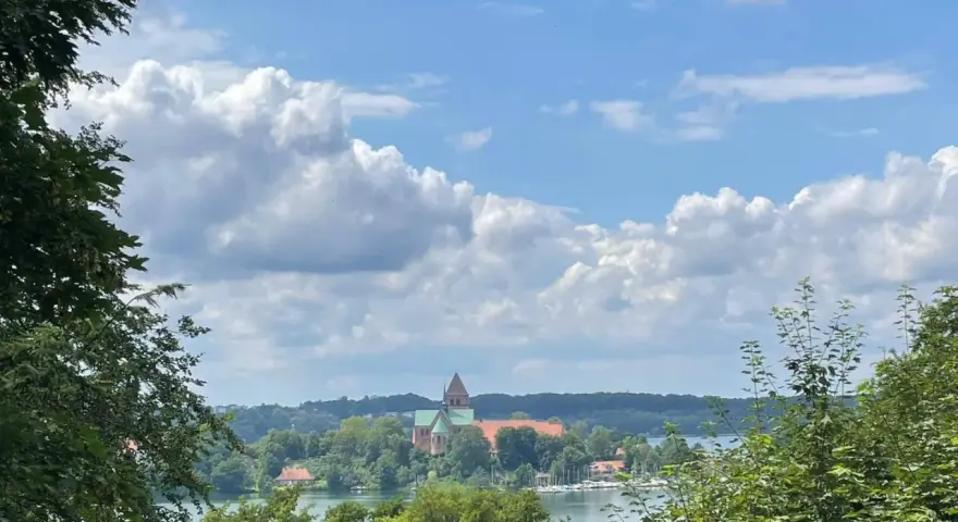 Blick auf die Ratzeburg Altstadt mit Domkirche, umgeben von grünen Bäumen und dem See unter einem dramatischen Wolkenhimmel.