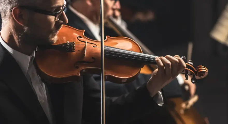 Skrzypek grający melodię, która mogłaby być jedną z piosenek o Krakowie. W tle inni muzycy orkiestry.