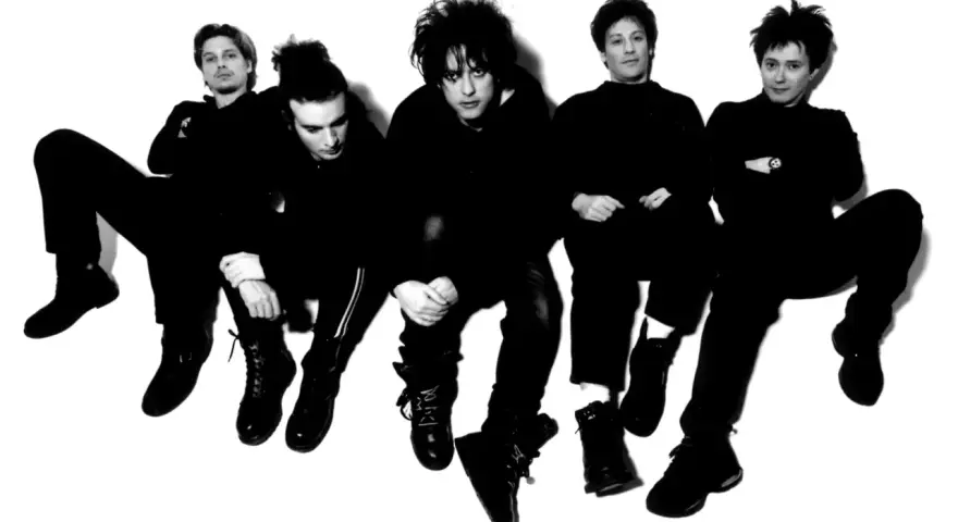 Les membres de The Cure, cinq silhouettes sombres aux coiffures distinctives, posent en groupe, l'air pensif.
