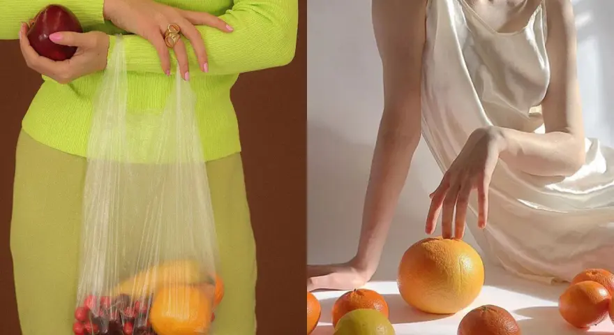 Mani che tengono una mela e una busta con ciliegie e arance. Altre arance e un limone sparsi su uno sfondo chiaro, evocando un'essenza di fruit extract.